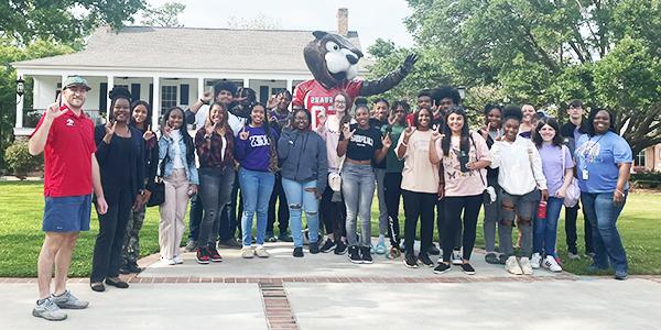 A group of students standing in front of Southpaw statue holding up the J sign for Jaguars.